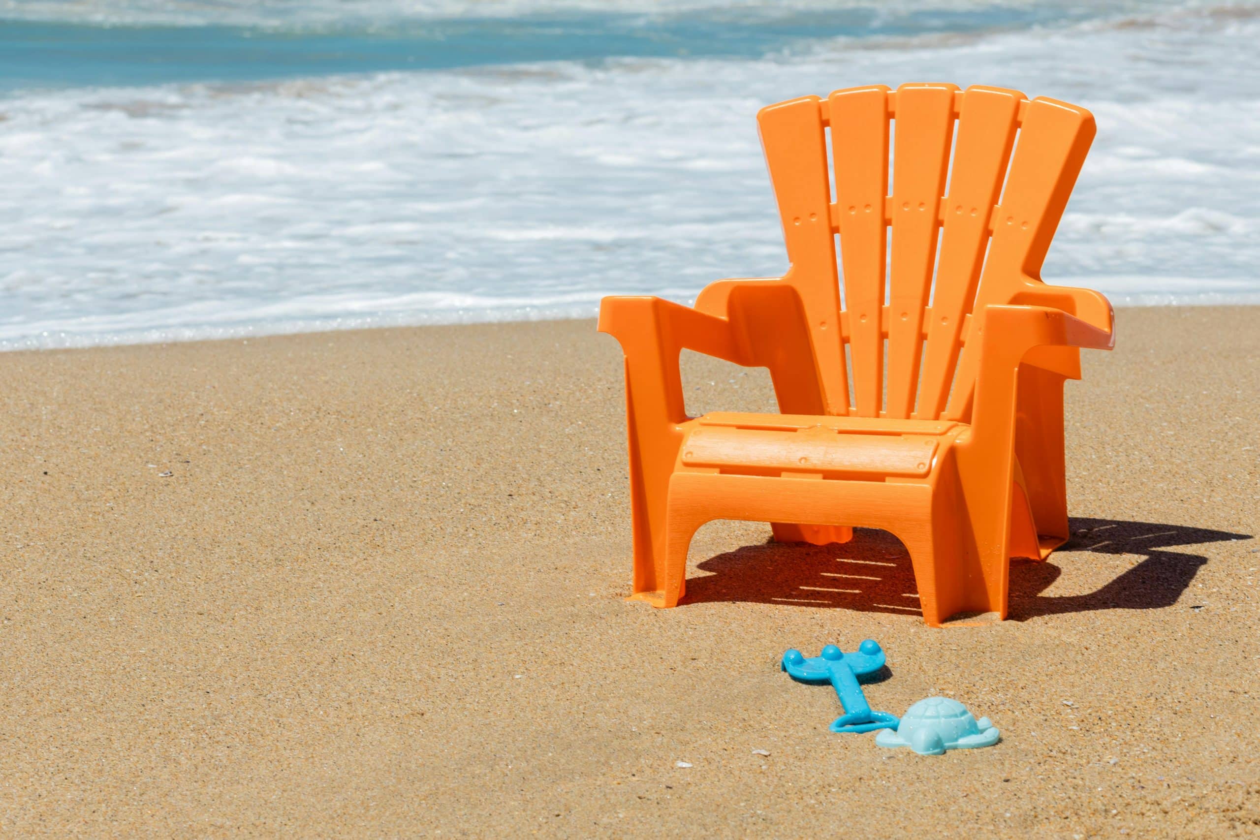 Orange chair and turquoise toys on a sunny beach, perfect for summer relaxation.